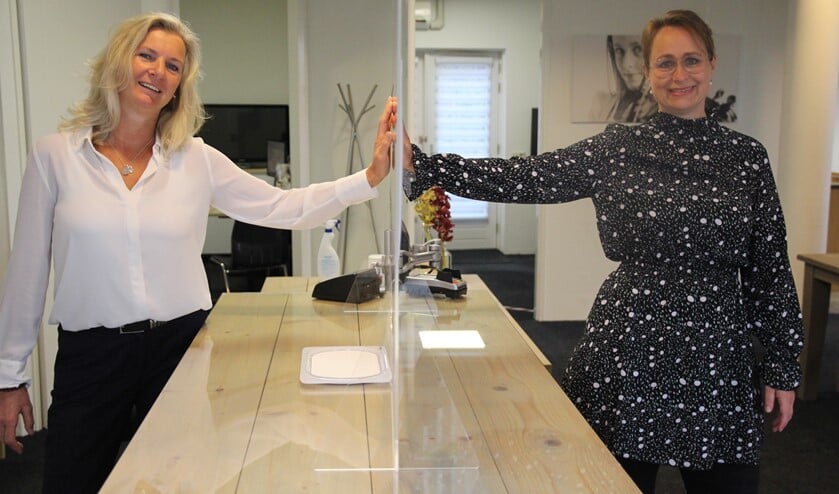 Dorothea en Eline bij het plexiglascherm dat bij de balie voor veiligheid zorgt.