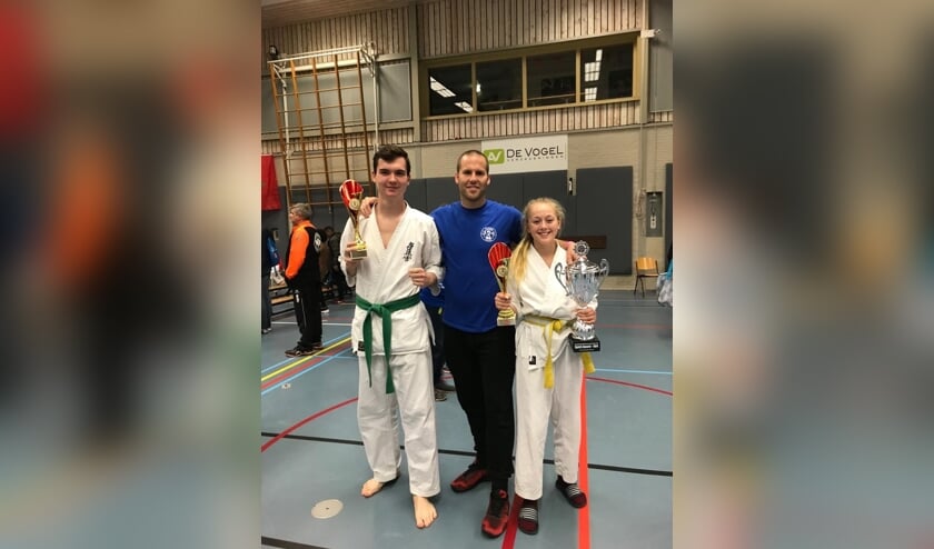 Bas van Brussel (links) en Jette Prins (rechts) met hun gewonnen beker met in hun midden trainer Jacques van Roosmalen.