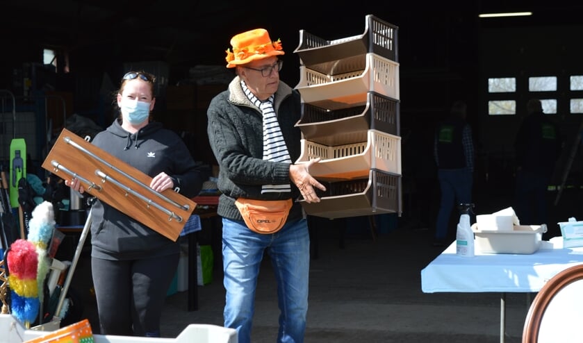 <p>De spreekstalmeester van de rommelmarkt helpt een klant met het sjouwen van haar aankopen.</p>