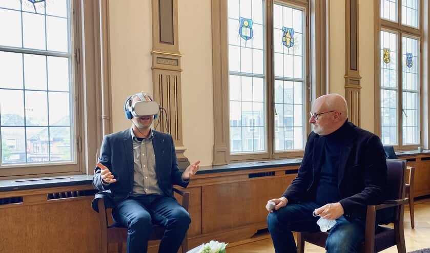 <p>Wethouder Roozendaal probeert de VR-bril uit, vrijwilliger Marcel kijkt toe.</p>