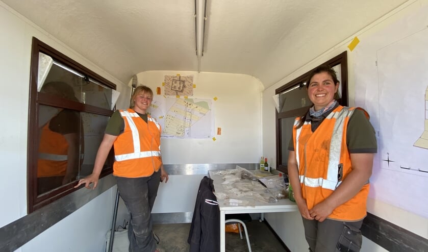 De archeologen Pleun Beurskens (achter) en Emma de Boo van Uijen tonen de vondsten. Op de achterwand overzichtskaarten waarop het kamp getekend is. (foto Jos Gröniger)