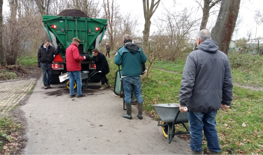 Vrijwilligers van de schooltuinen halen kruiwagen na kruiwagen compost die vervolgens over de tuinen wordt uitgespreid. | Foto: PR