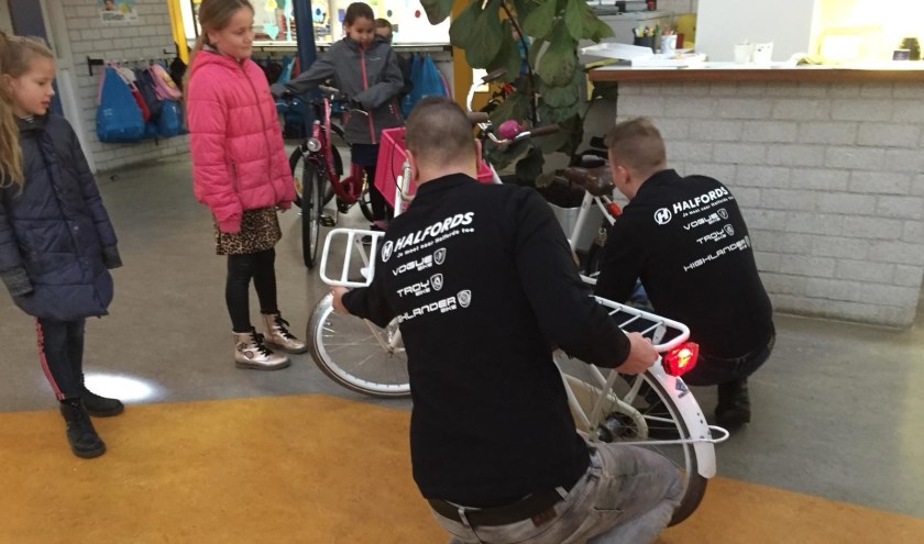 De mannen van Halfords checken een fiets terwijl de eigenares geïnteresseerd toekijkt.