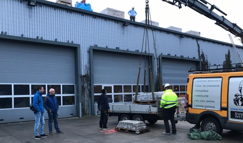Bestuursleden Coen Huisman en Lodewijk van Aernsbergen van Zon op Leiderdorp kijken toe hoe de medewerkers van Freek van Os alle benodigde materialen op het dak takelen.