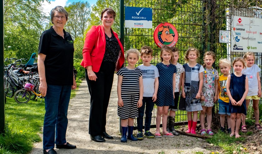 Wethouder Angelique Beekhuizen (met rood jasje) heeft, onder toeziend oog van een groep speeltuingebruikertjes, het bord 'Rookvrij' onthuld. Links voorzitter Riny Vons van de Stichting Natuurspeeltuin Leiderdorp.