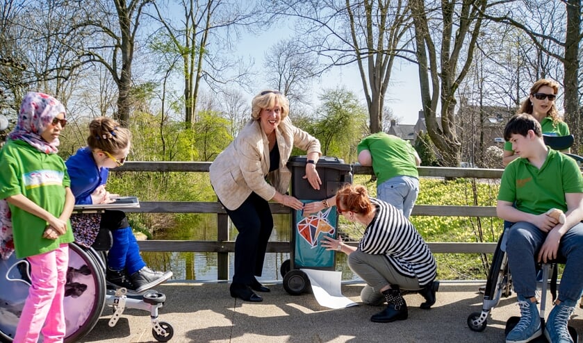 <p>Burgemeester Driessen en Elke van Geest beplakken een afvalcontainer met een van de fraaie stickers. Nafiso, Nadja, Wesley en Anne kijken toe.</p>